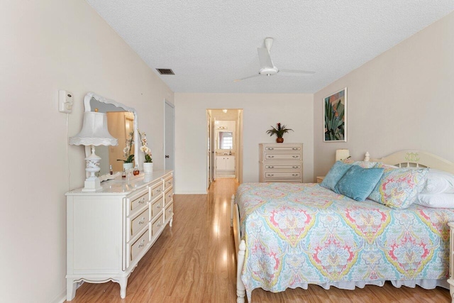 bedroom with ceiling fan, ensuite bathroom, light hardwood / wood-style flooring, and a textured ceiling