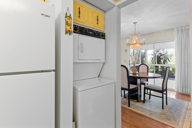 laundry area with a notable chandelier, light hardwood / wood-style floors, stacked washer and clothes dryer, and a textured ceiling