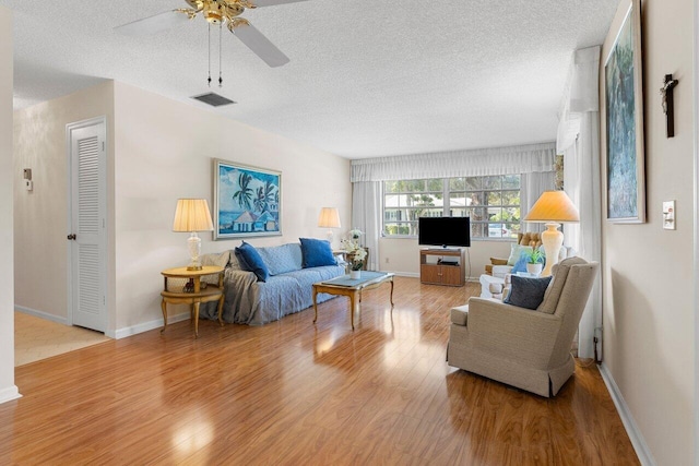 living room with ceiling fan, a textured ceiling, and light wood-type flooring