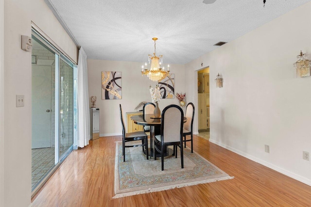 dining area with a notable chandelier, a textured ceiling, and light wood-type flooring