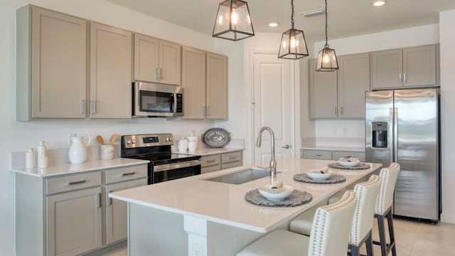 kitchen featuring gray cabinets, sink, a kitchen bar, a kitchen island with sink, and stainless steel appliances