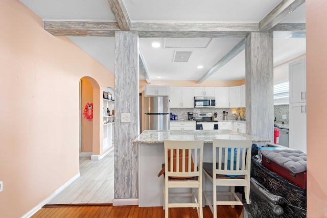 kitchen with a breakfast bar area, stainless steel appliances, light stone countertops, white cabinets, and decorative backsplash