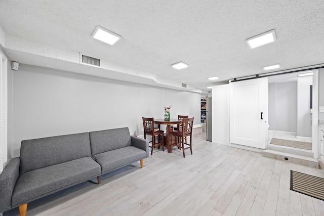 living room featuring a barn door, a textured ceiling, and light hardwood / wood-style flooring