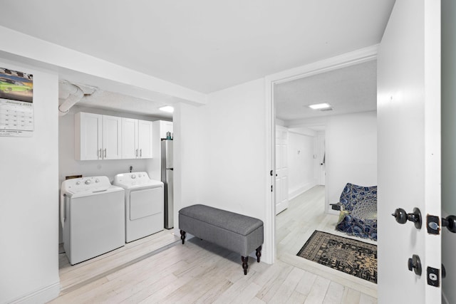 laundry room with separate washer and dryer, light hardwood / wood-style floors, and cabinets