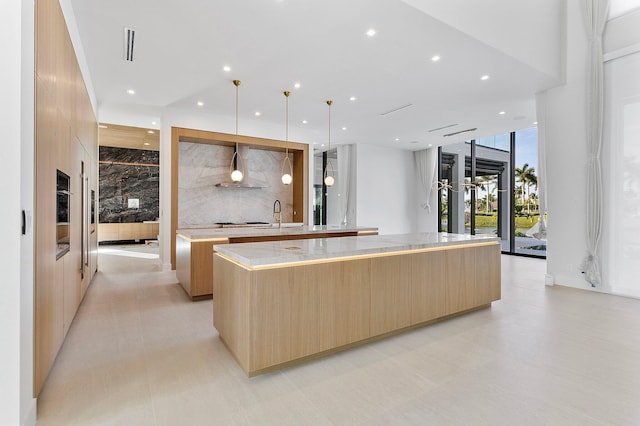 kitchen featuring light brown cabinetry, decorative light fixtures, sink, a large island, and floor to ceiling windows