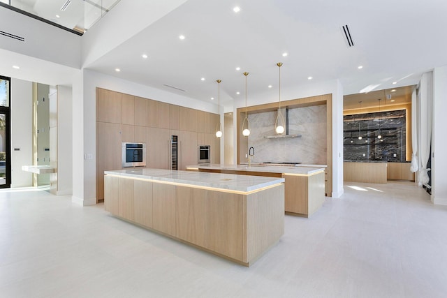 kitchen featuring pendant lighting, a large island, wall chimney range hood, sink, and light brown cabinets