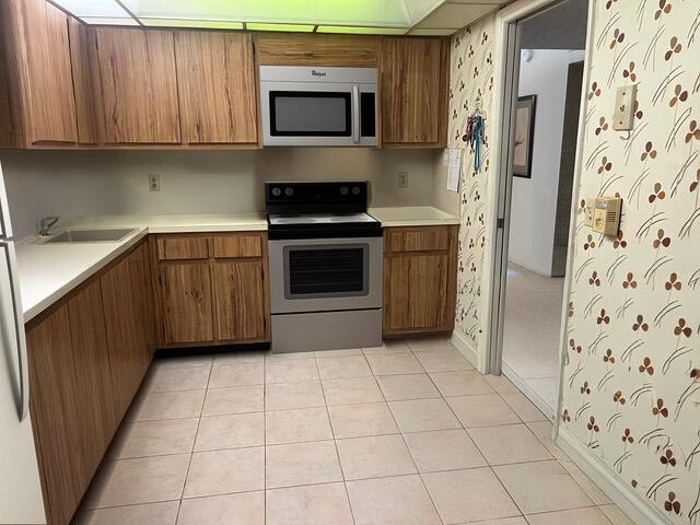 kitchen with stainless steel appliances, brown cabinets, a sink, wallpapered walls, and light countertops