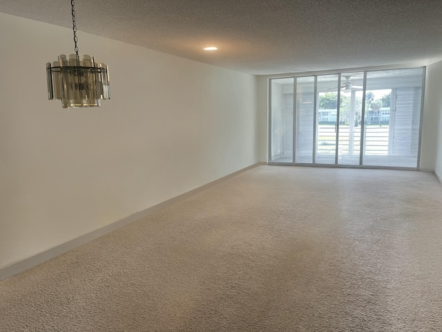 empty room with a textured ceiling, a chandelier, carpet floors, and floor to ceiling windows