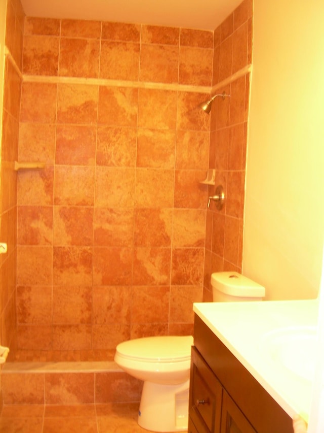 bathroom featuring vanity, a tile shower, and toilet