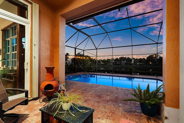 pool at dusk with a patio, a fireplace, and glass enclosure