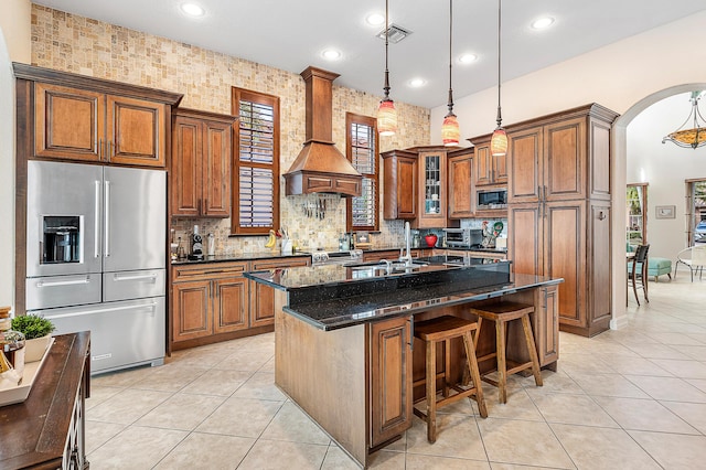 kitchen featuring hanging light fixtures, dark stone countertops, appliances with stainless steel finishes, a kitchen island, and custom range hood