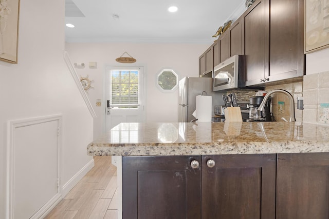kitchen with stainless steel microwave, decorative backsplash, freestanding refrigerator, a peninsula, and dark brown cabinets