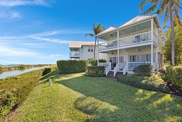 back of house featuring a balcony, metal roof, a water view, ceiling fan, and a yard