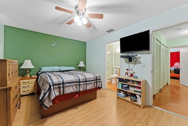 bedroom with ceiling fan, ensuite bath, a textured ceiling, and light wood-type flooring