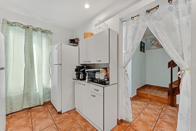 kitchen with white refrigerator, light tile patterned flooring, and white cabinets