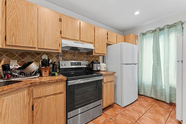 kitchen featuring freestanding refrigerator, decorative backsplash, light brown cabinetry, under cabinet range hood, and stainless steel electric stove
