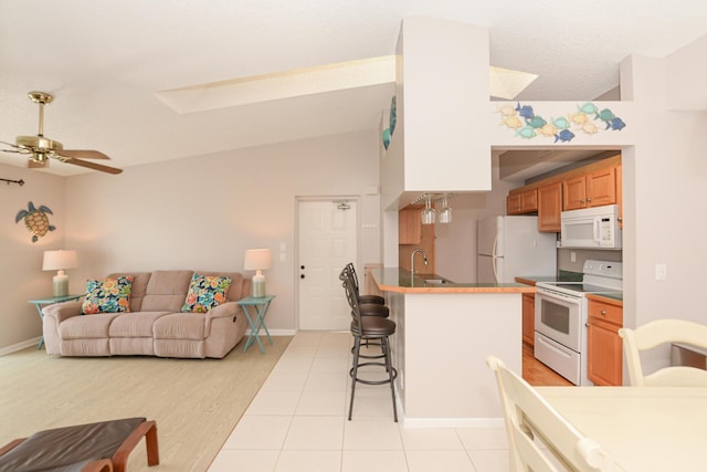 kitchen with vaulted ceiling with skylight, sink, a kitchen breakfast bar, ceiling fan, and white appliances