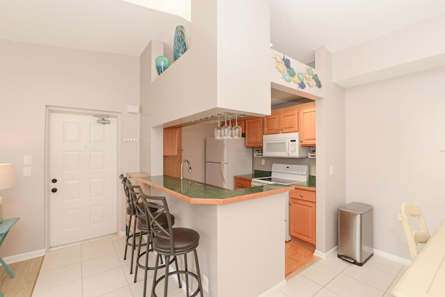 kitchen with a kitchen bar, a textured ceiling, light tile patterned floors, kitchen peninsula, and white appliances