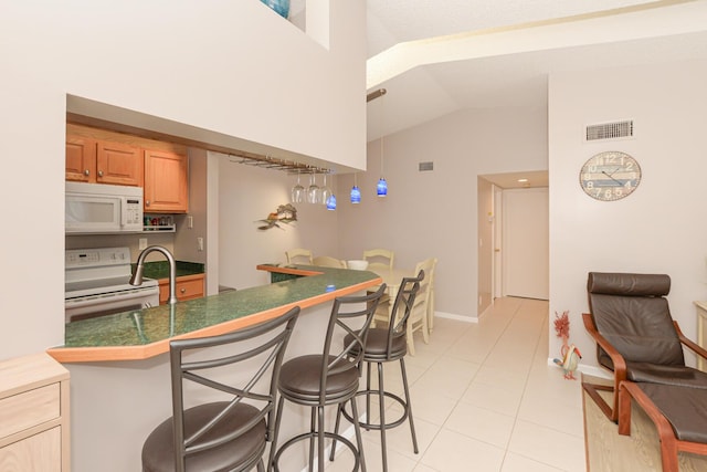 kitchen featuring light tile patterned floors, white appliances, a breakfast bar area, high vaulted ceiling, and kitchen peninsula