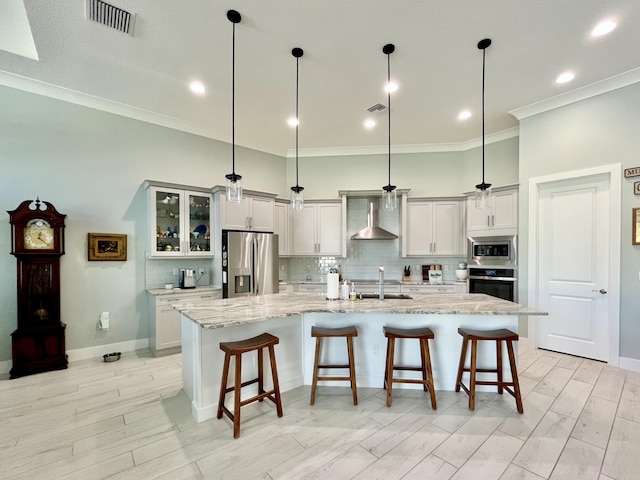 kitchen with pendant lighting, wall chimney range hood, a large island with sink, and appliances with stainless steel finishes