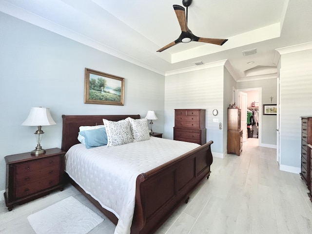 bedroom with ceiling fan, ornamental molding, a raised ceiling, and light hardwood / wood-style flooring