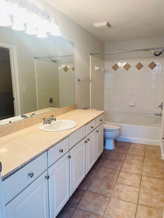 full bathroom featuring tiled shower / bath, vanity, toilet, tile patterned floors, and a textured ceiling