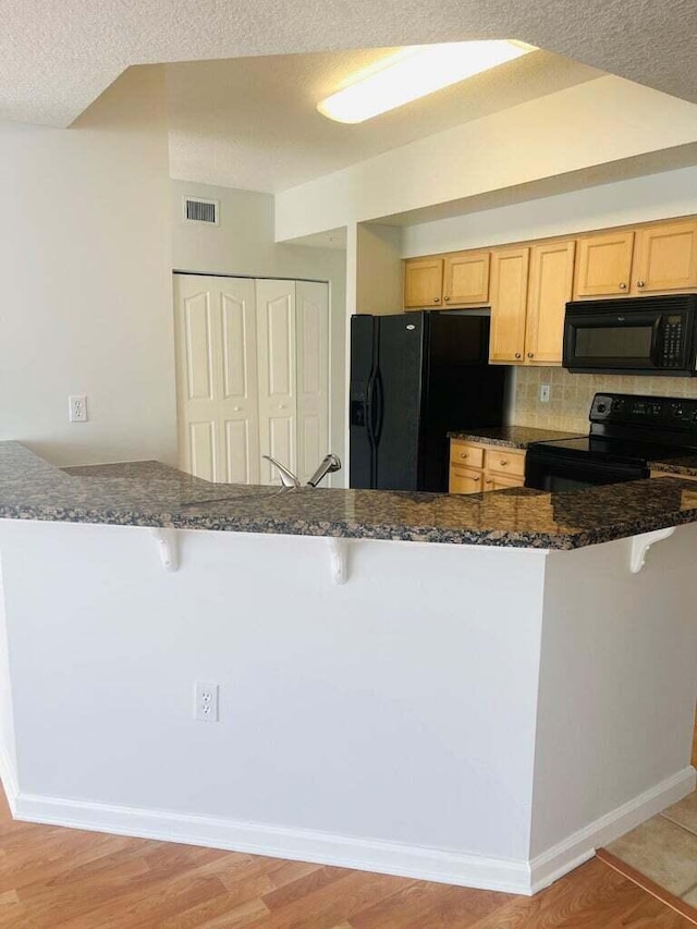 kitchen featuring light brown cabinets, kitchen peninsula, a kitchen breakfast bar, and black appliances