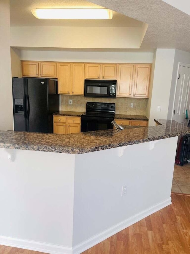 kitchen with tasteful backsplash, light brown cabinetry, black appliances, and light wood-type flooring