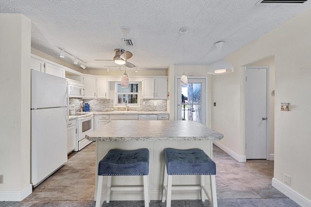 kitchen featuring a kitchen island, decorative light fixtures, white cabinetry, sink, and white appliances