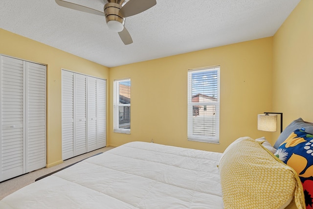 carpeted bedroom featuring multiple closets, ceiling fan, a textured ceiling, and multiple windows