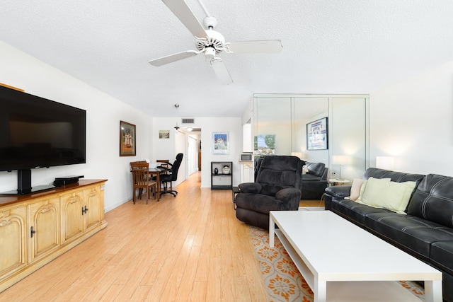 living room featuring ceiling fan, a textured ceiling, and light hardwood / wood-style floors