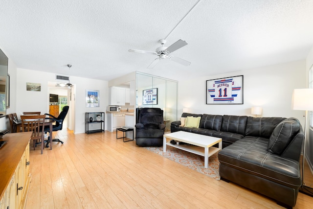 living room with ceiling fan, a textured ceiling, and light wood-type flooring