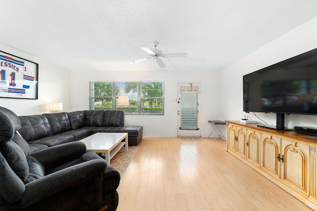 living room with ceiling fan, a textured ceiling, and light wood-type flooring