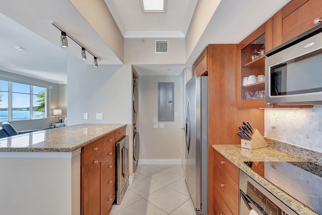 kitchen featuring stacked washer / drying machine, light stone counters, appliances with stainless steel finishes, kitchen peninsula, and decorative backsplash