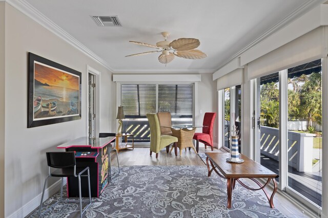 living room featuring ceiling fan, ornamental molding, a stone fireplace, and light hardwood / wood-style floors