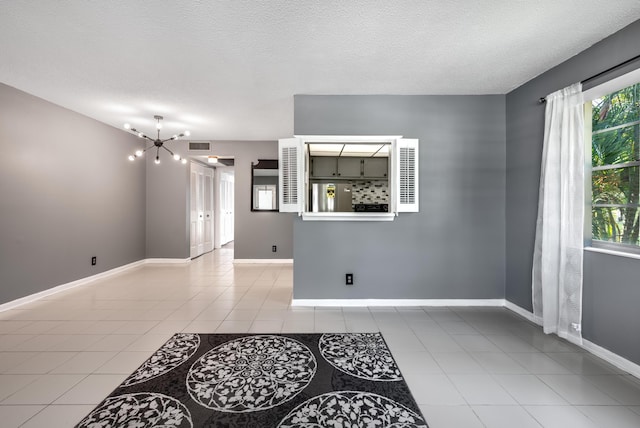 tiled spare room with a textured ceiling and a notable chandelier