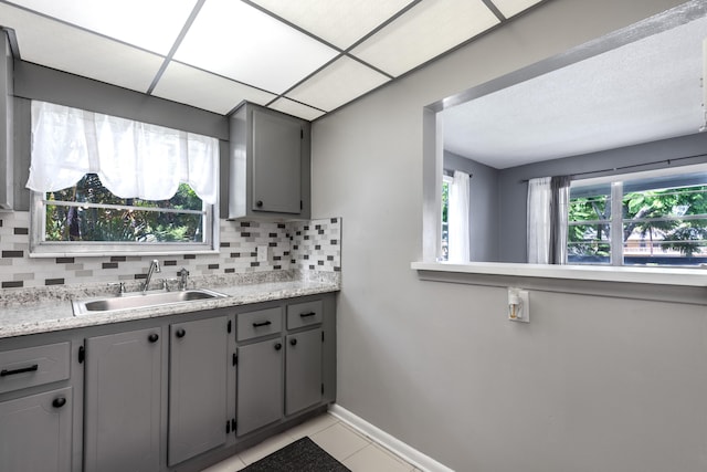 kitchen featuring sink, tasteful backsplash, light tile patterned floors, gray cabinets, and a drop ceiling