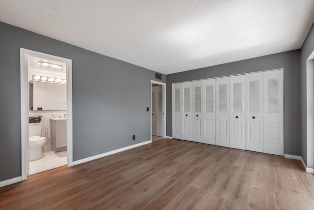 unfurnished bedroom with connected bathroom, a textured ceiling, and light wood-type flooring