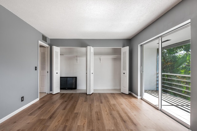 unfurnished bedroom with access to exterior, two closets, wood-type flooring, and a textured ceiling