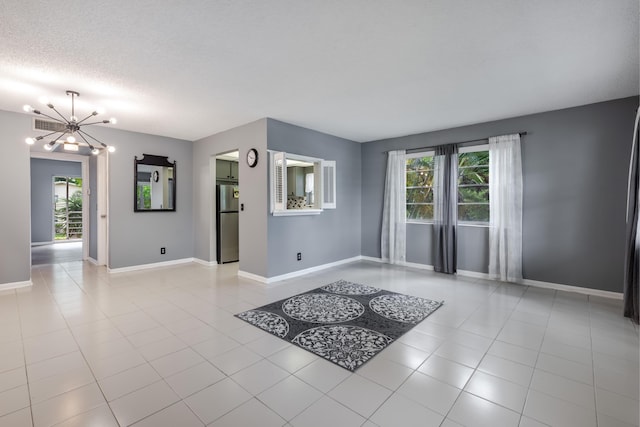 empty room featuring an inviting chandelier, plenty of natural light, a textured ceiling, and light tile patterned floors