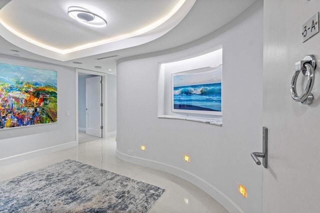 hallway featuring a tray ceiling and light tile patterned floors