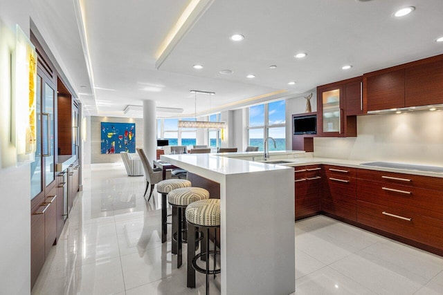 kitchen with a breakfast bar, sink, light tile patterned floors, pendant lighting, and black electric stovetop