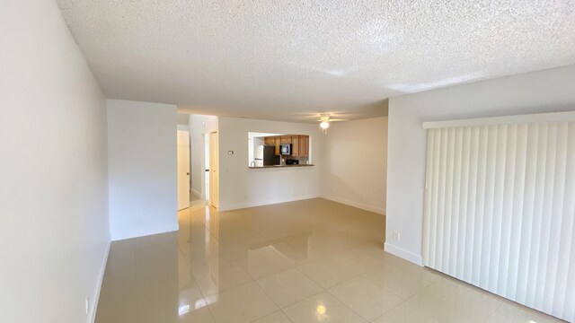 spare room with light tile patterned floors, baseboards, a textured ceiling, and a ceiling fan