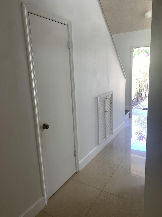 hallway featuring light tile patterned flooring, a textured ceiling, and baseboards