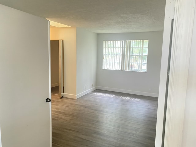 unfurnished room featuring a textured ceiling, dark wood-type flooring, and baseboards