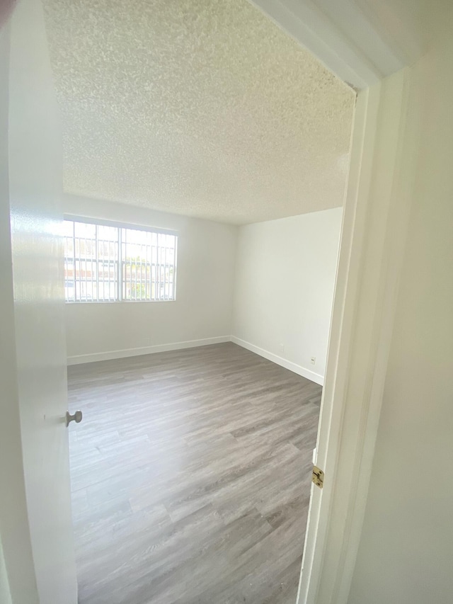 spare room with a textured ceiling, baseboards, and wood finished floors