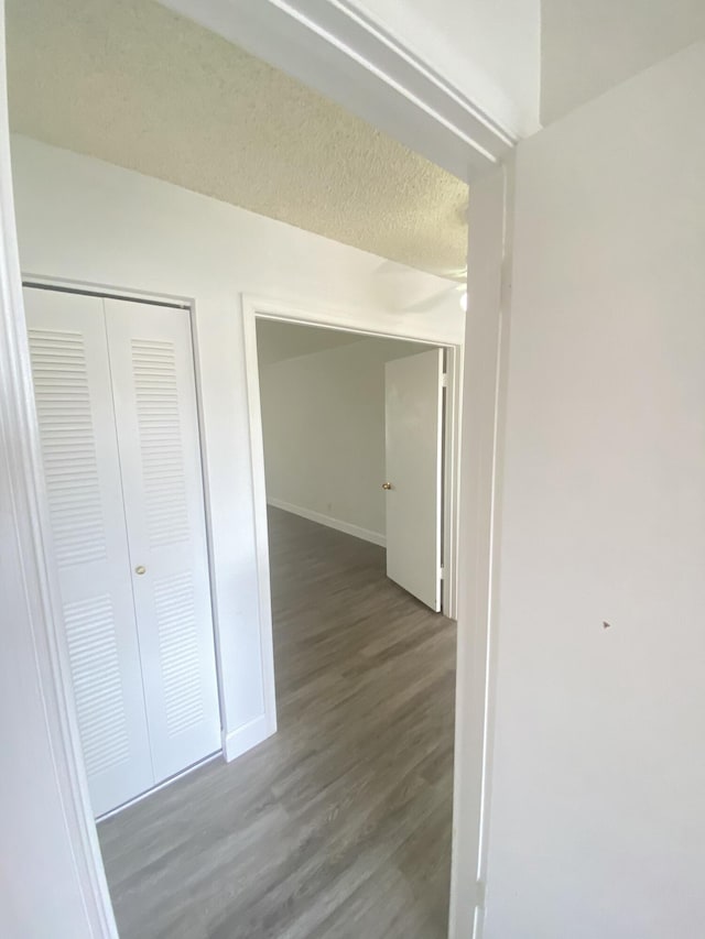 corridor featuring wood finished floors, baseboards, and a textured ceiling