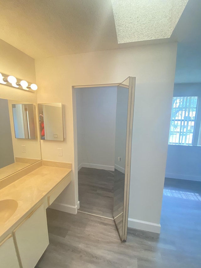 bathroom with vanity, wood finished floors, baseboards, and a textured ceiling