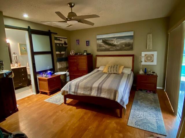 bedroom with ceiling fan, a barn door, a textured ceiling, and light hardwood / wood-style flooring