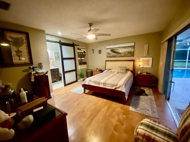 bedroom with light wood-type flooring, a barn door, a textured ceiling, and ceiling fan